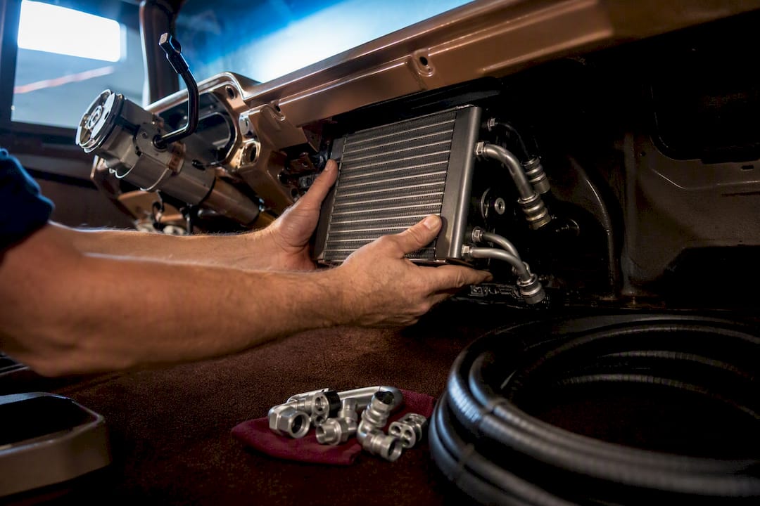 Hands fitting AC components beneath classic dashboard